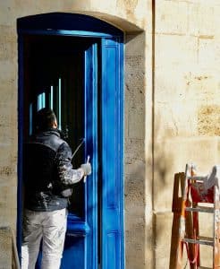 Peintre en pleine peinture d'une porte en bois ancienne de couleur bleu